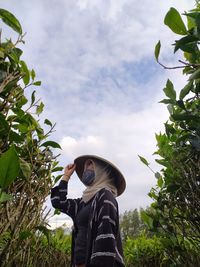 Low section of man holding plants against sky