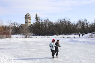 People on snow field by building against sky