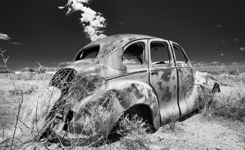 Abandoned car on field against sky