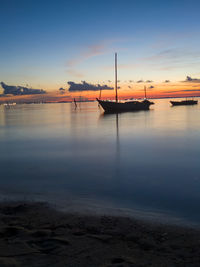 Sailboats moored on sea against sky during sunset