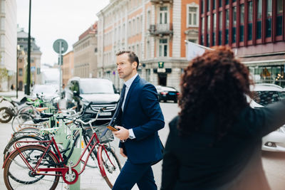 Side view of businessman walking by businesswoman on sidewalk in city