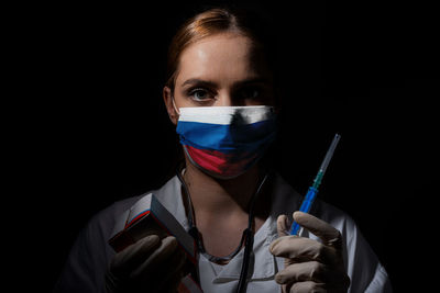 Portrait of young woman holding camera over black background