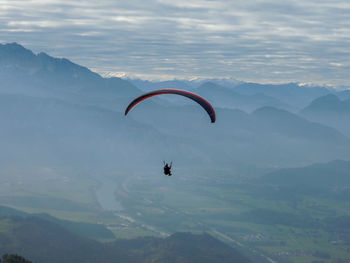 Person paragliding over mountains against cloudy sky