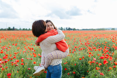 Mother holding a daughter in arms in a field full of poppies flowers