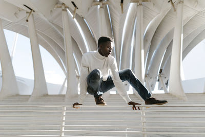 Young man in white turtleneck sitting on railing