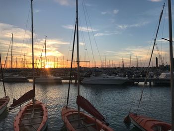 Sailboats moored at harbor against sky during sunset