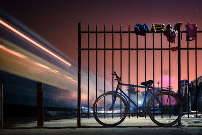 Bicycle parked by fence on railroad station platform at night