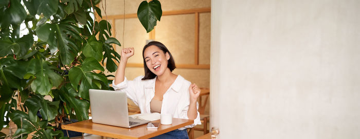 Side view of young woman using laptop while standing against wall