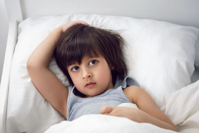 Child boy lies in a white children's bed with a blanket in a room with toy rabbit