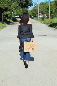 Rear view of woman with message walking on road in city