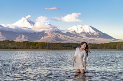 Young woman looking away while standing in lake against snowcapped mountain