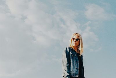 Portrait of young woman wearing sunglasses standing against sky