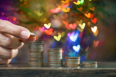 Close-up of cropped hand stacking coins on table against defocused lights