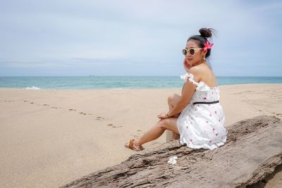 Portrait of woman wearing sunglasses while sitting at beach against sky