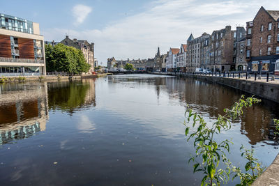 Canal by buildings in city against sky