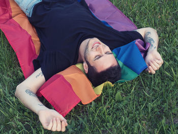 High angle view of man lying on rainbow flag at grassy field