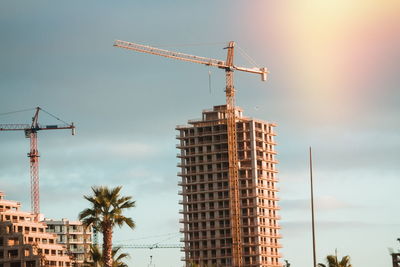 Low angle view of crane by building against sky