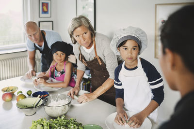 Family looking at woman while preparing food in kitchen