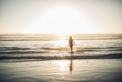 Man walking on beach against sky during sunset