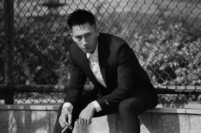 Portrait of young man sitting against chainlink fence