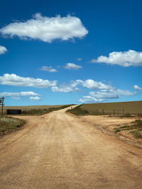 Dirt road on field against sky