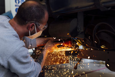 Mechanic wearing protective face mask cutting metal of car in auto garage