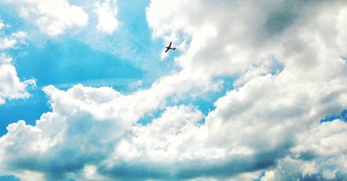 Low angle view of airplane flying against cloudy sky