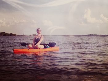 Young woman sitting in sea against sky