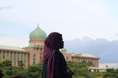 Side view of woman wearing hijab standing against mosque