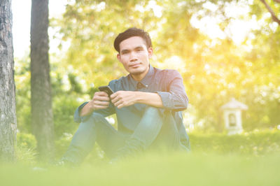 Young man using smart phone while sitting on land