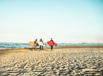 Rear view of friends walking with surfboards at beach on sunny day