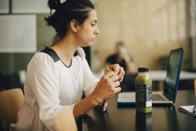 Businesswoman eating food and having healthy drink while using laptop at office desk