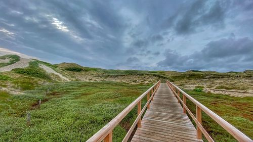 Boardwalk leading towards landscape against sky