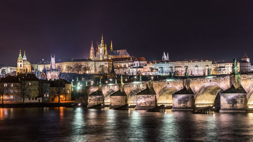 Illuminated bridge over river against buildings in city at night