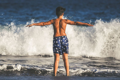 Rear view of shirtless man standing on beach