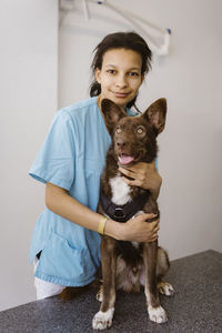 Portrait of female nurse embracing dog on examination table in medical clinic