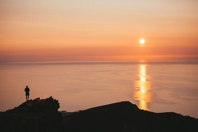 Silhouette man looking at sea against sky during sunset