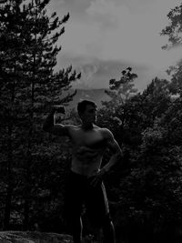 Shirtless man flexing muscles while standing on field against sky