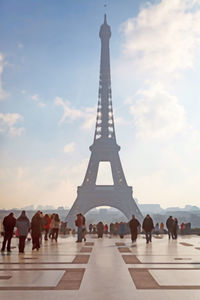 People walking in front of tower against sky