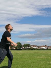 Playful man on grassy field against sky