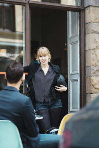 Businesswoman holding helmet while talking to colleague at sidewalk cafe