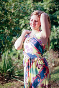 Smiling young woman looking away while standing against trees