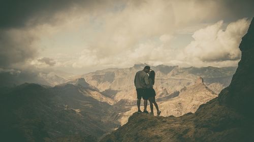 Couple kissing while standing against mountain range