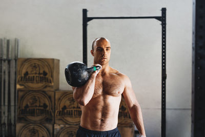 Shirtless young man exercising with kettlebell in gym