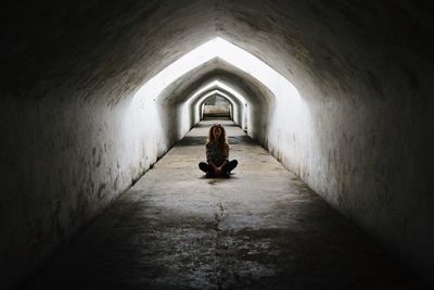 Woman sitting on cross in corridor