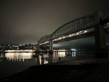 Illuminated bridge over river against sky at night