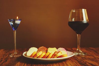 Close-up of cheese in plate by wineglass on table