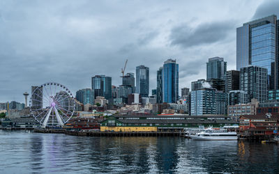 Buildings by river against cloudy sky