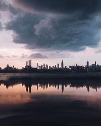 Silhouette buildings by lake against sky during sunset