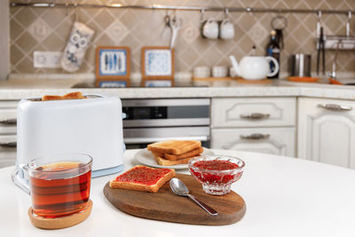 White toaster, cup of black tea, stack of toasted bread, crispy toast with raspberry jam